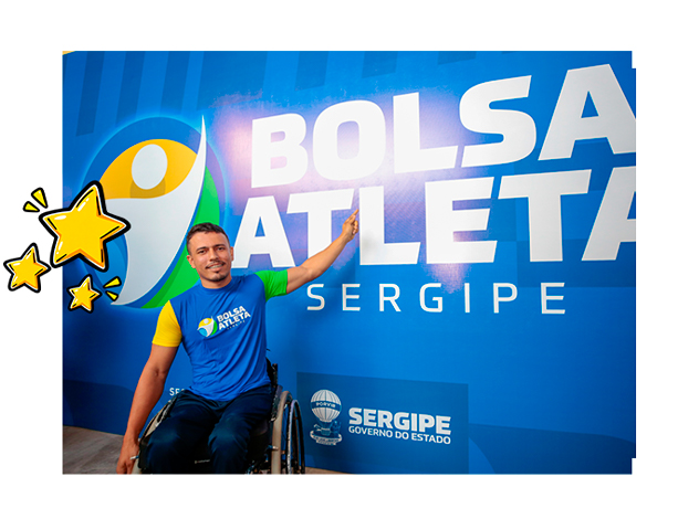 Atleta paralímpico em cadeira de rodas em frente ao painel do Bolsa Atleta Sergipe
